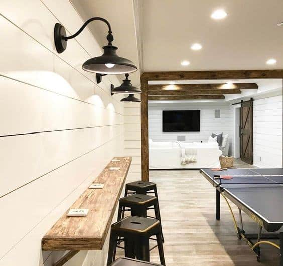 Basement with shiplap walls, rustic wooden bar, wall sconces, and ping pong table.