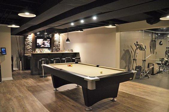 Modern basement with pool table, bar area, gym equipment, and industrial-style pendant lights.