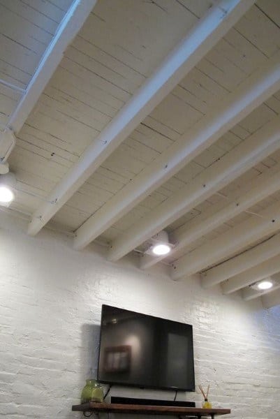 Basement with white exposed beams, brick walls, and recessed spotlights.