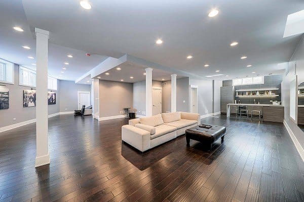 Spacious modern basement with dark wood flooring, sectional sofa, and recessed lighting.