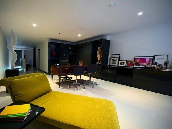 Modern basement office with yellow chaise lounge, black cabinets, and recessed lighting.