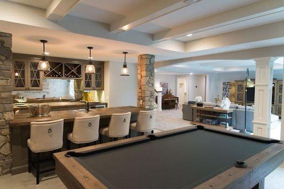 Basement bar with stone accents, black pool table, beige stools, and rustic pendant lights.