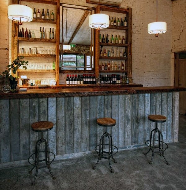 Rustic bar with wooden stools, mirrored backdrop, shelves of bottles, and pendant lights; a cozy atmosphere