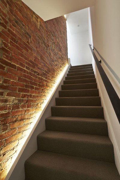 Modern basement staircase with exposed brick wall and sleek under-rail lighting.