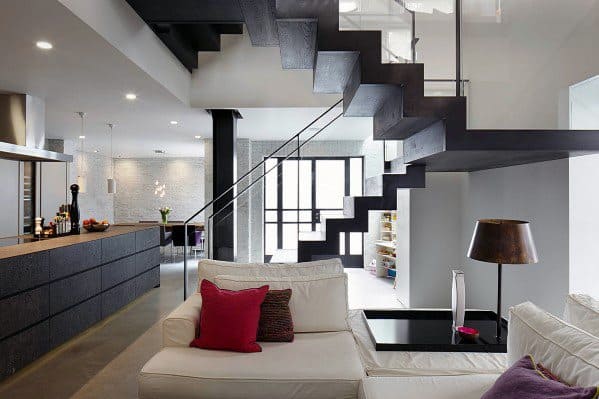 Modern black floating staircase with glass railing in an open-plan living area.