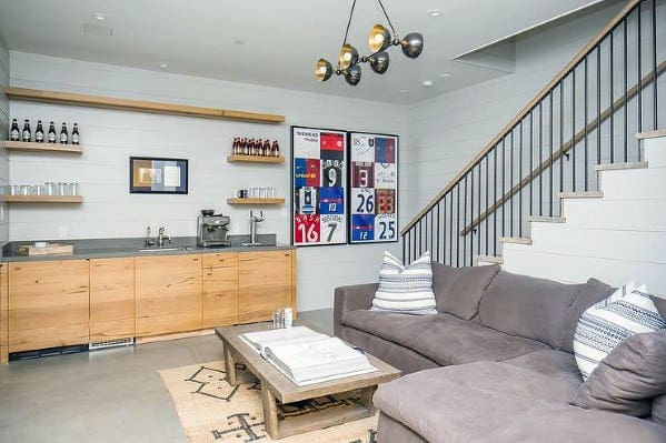 Modern basement lounge with staircase featuring black vertical railing and wooden cabinetry.