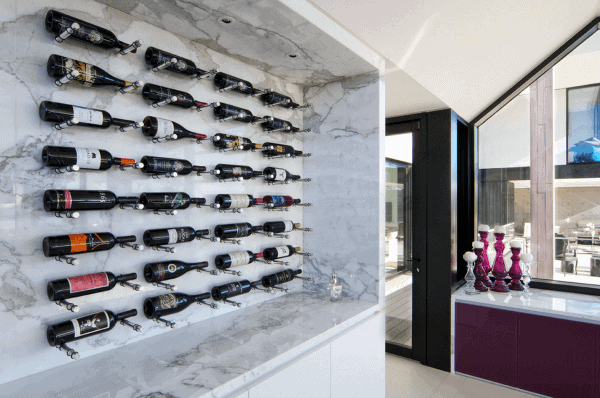 Modern wine rack with various wine bottles on a marble wall, overlooking a patio through large glass windows