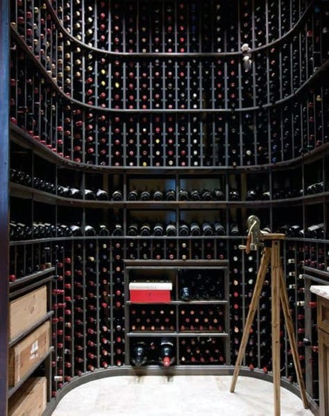 Cellar with floor-to-ceiling wine racks filled with wine bottles and a wooden tripod stand in the center