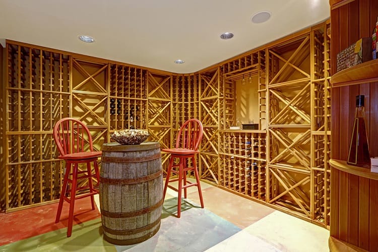 Wine cellar with wooden racks, a barrel table, and red chairs, creating a cozy tasting area.