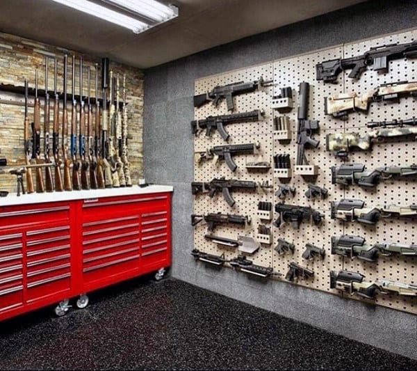 Gun room featuring a red tool chest workbench, pegboard walls displaying firearms, and a stone accent rifle rack.