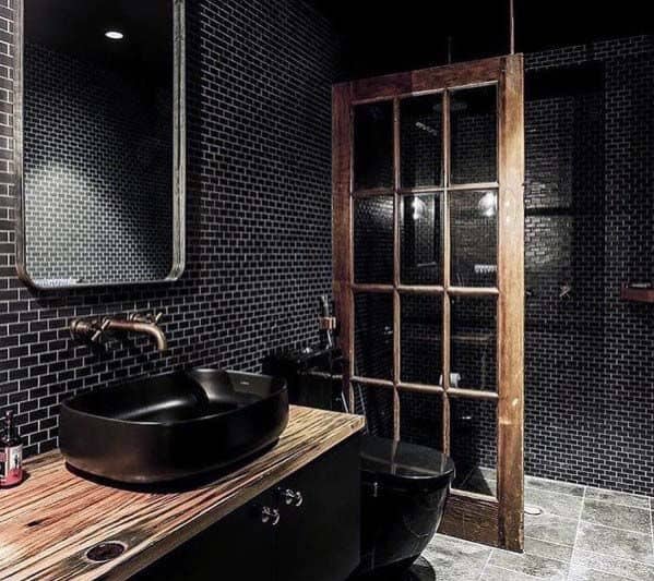 Modern black bathroom with mosaic tiles, wooden accents, and a glass-panel door.