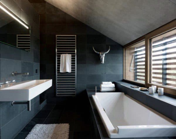 Modern bathroom with concrete ceiling, black tiled walls, and minimalist bathtub.