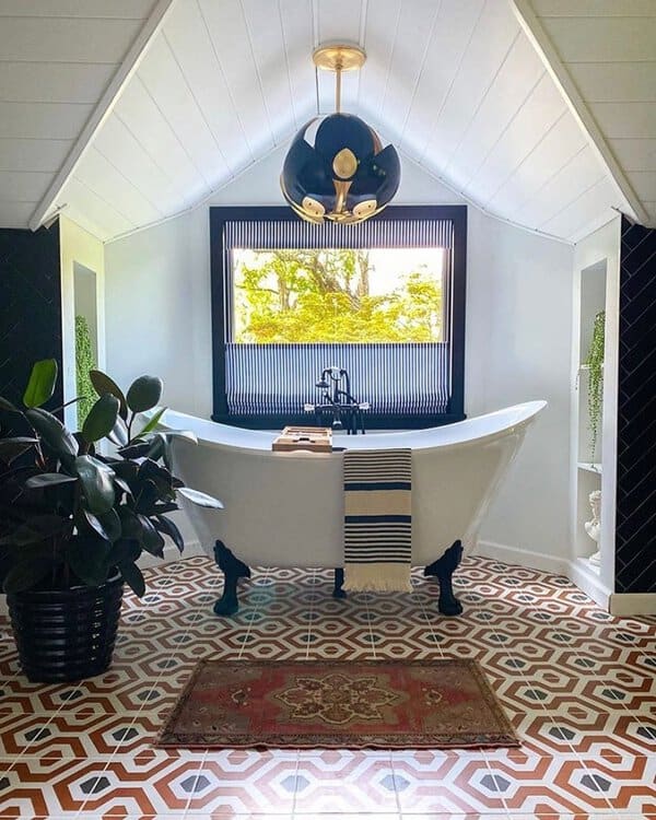 Black-and-gold pendant above a white clawfoot tub with bold geometric tile in a bright attic bathroom.
