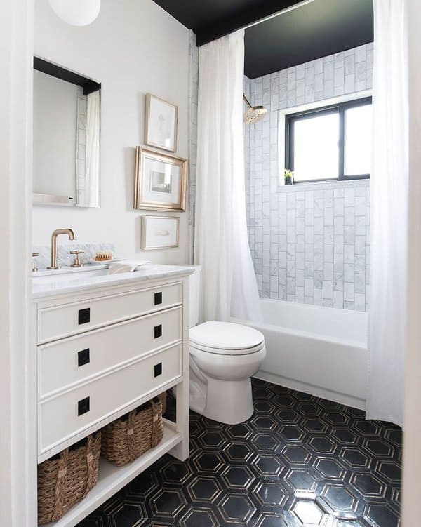 Small bathroom with marble tiles, white vanity, black hexagonal floor tiles, and white shower curtain.