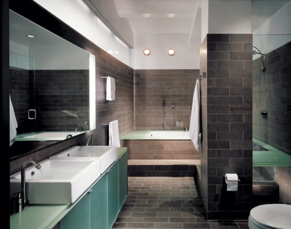 Modern bathroom with double sink vanity, bathtub, and dark tiled walls and floors