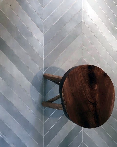 Chevron-patterned light gray floor tiles with a rustic wooden stool.