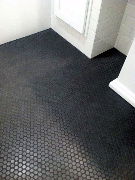 Black hexagonal non-slip rubber flooring in a modern bathroom with white tiled walls.