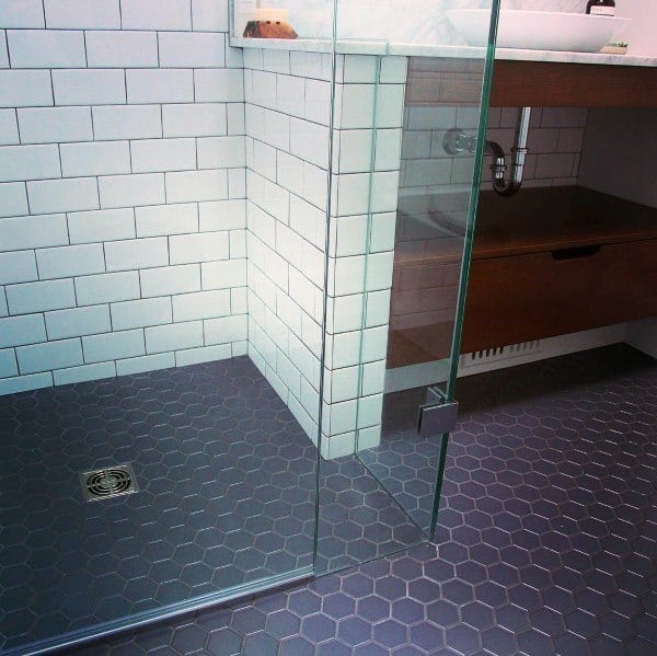 Bathroom with gray hexagonal honeycomb floor tiles, subway tile walls, and a glass shower enclosure.