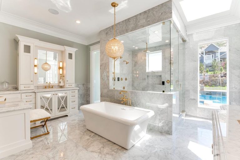 Beaded globe chandelier above a white tub in a marble bathroom, accented by gold fixtures and elegant white cabinetry.