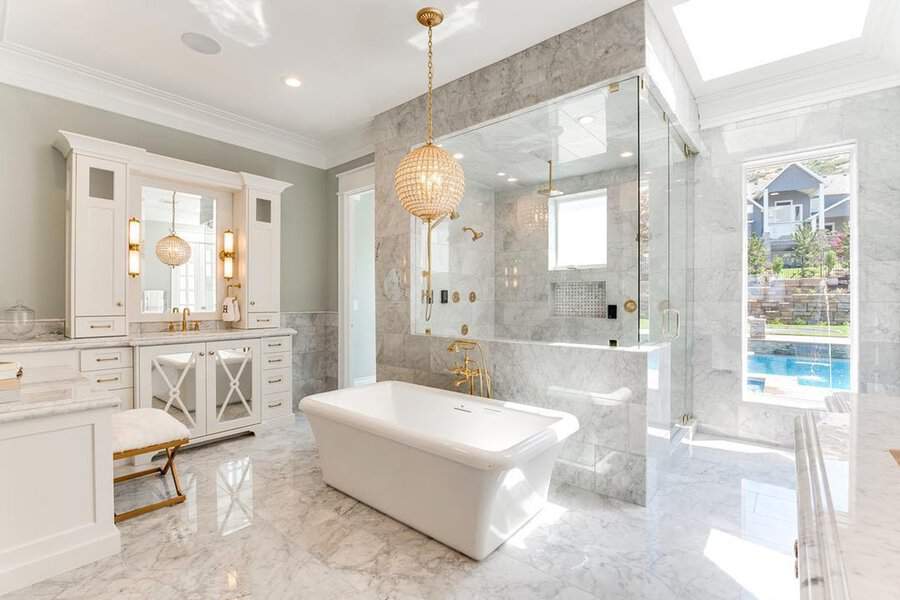 Beaded globe chandelier above a white tub in a marble bathroom, accented by gold fixtures and elegant white cabinetry.