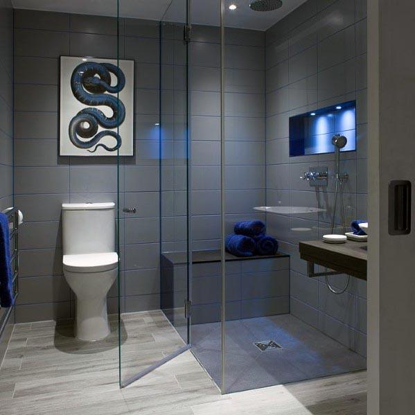 A modern grey bathroom featuring sleek tiled walls, a walk-in shower with glass enclosure, a minimalist vanity, and blue accent lighting.