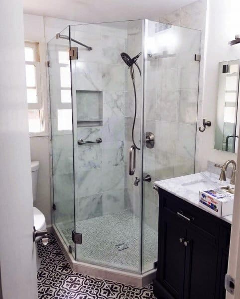 Modern bathroom with a glass shower in the corner, white marble walls, dark vanity, and patterned floor tiles