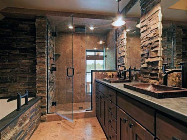 Rustic bathroom with stone walls, glass shower, dual rustic sinks, and modern fixtures