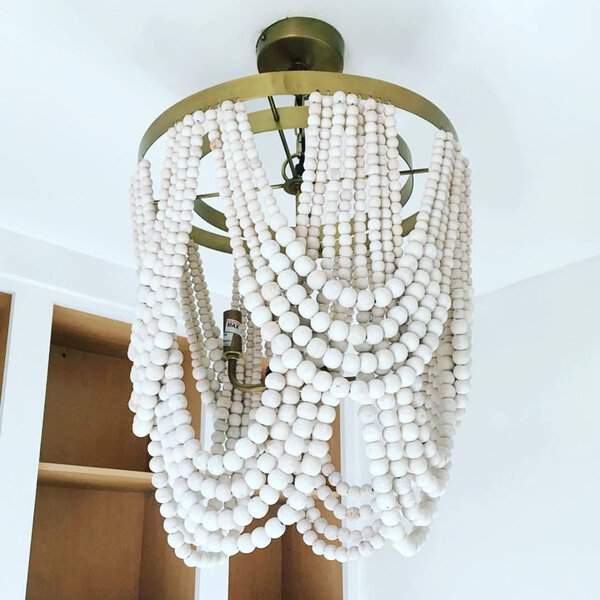 White beaded chandelier on a brass frame in a bright space, adding a warm, bohemian touch.