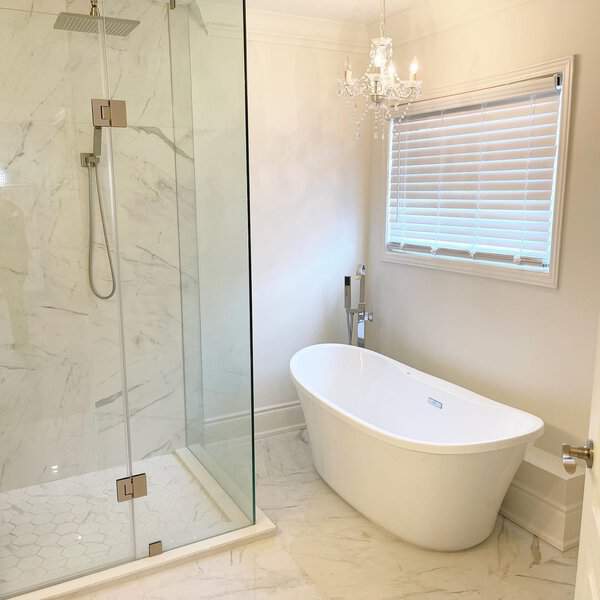 Small crystal chandelier above a white freestanding tub, marble surfaces, and a clear glass shower in a bright bathroom.