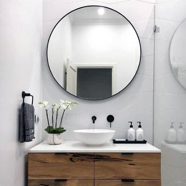 Minimalist bathroom with round mirror, vessel sink, and wooden vanity.