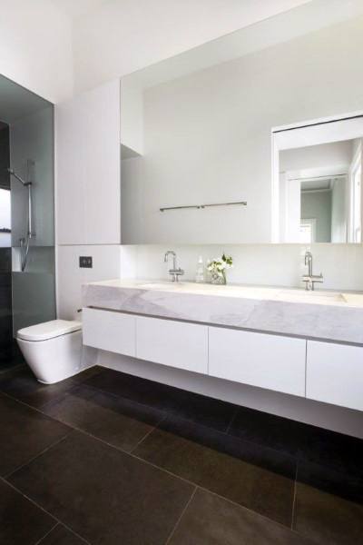 Minimalist bathroom with floating vanity, large wall-to-wall mirror, and dark floor tiles.