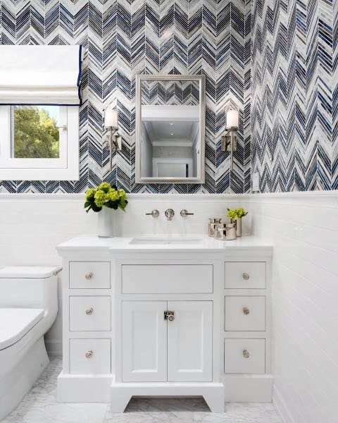 Bathroom with metallic-framed mirror, white vanity, and blue chevron-patterned wallpaper.