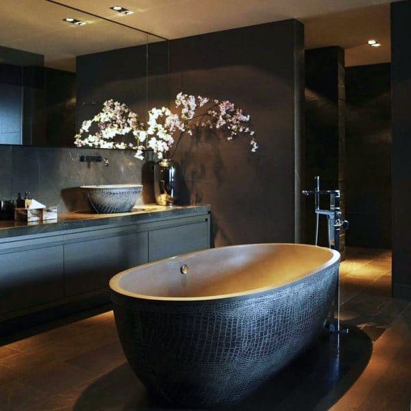 Luxury bathroom with freestanding textured bathtub, dark walls, and floral decor.