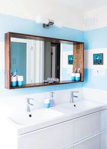Modern bathroom with wood-framed mirror, double sinks, and light blue walls.