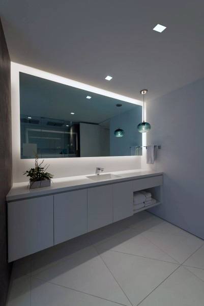 Sleek modern bathroom with large LED backlit mirror, floating vanity, and pendant lights.