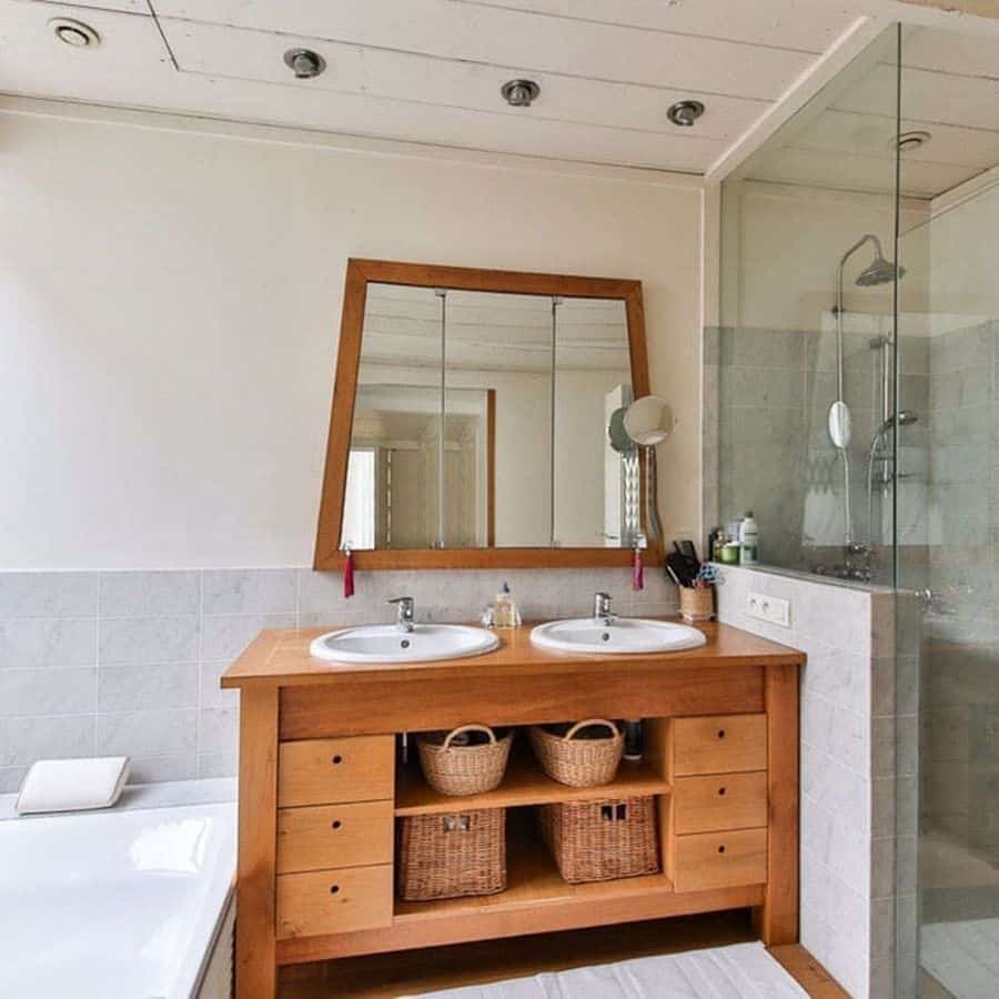 Modern bathroom with double sinks, wooden vanity, wicker baskets, and glass shower enclosure.