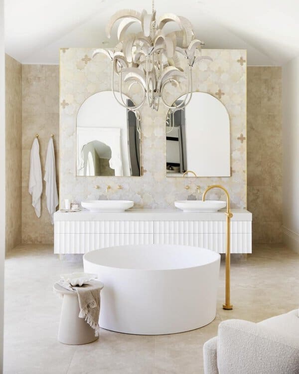Palm-like chandelier above a round soaking tub, fluted vanity, and Moroccan-inspired tile in a bright, spa-like bathroom.