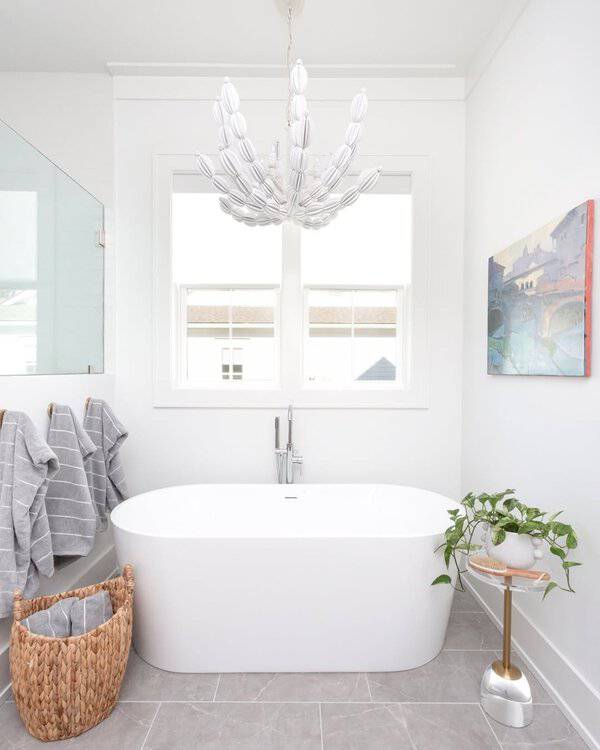 White petal chandelier above a sleek freestanding tub in a bright, minimal bathroom with gray floor tile.