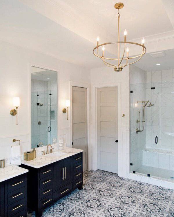 Ring-style gold chandelier above black-and-marble vanity, patterned floor tile, and a glass shower in a crisp, modern bathroom.