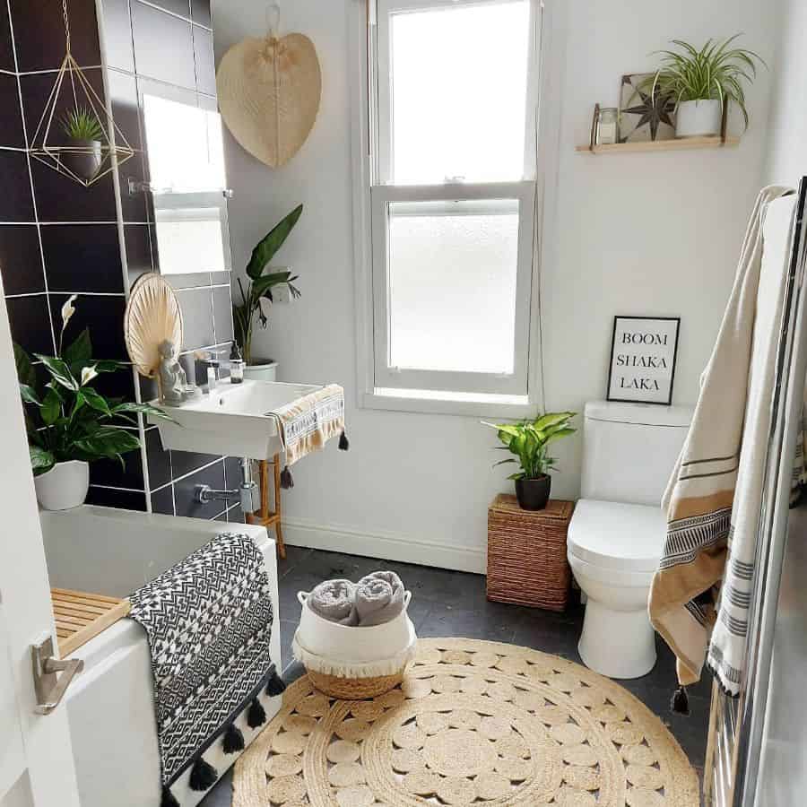 Modern bathroom with plants, woven rug, black tile, and "Boom Shaka Laka" wall art.