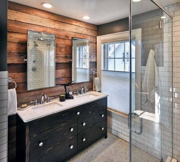 Rustic bathroom with dual sinks, wood paneling, glass shower, and white tiles
