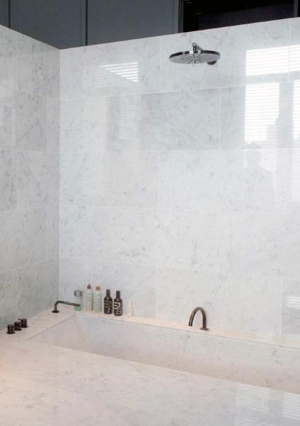 Luxurious white marble bathroom with built-in bathtub and modern showerhead.