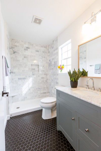 Bright bathroom with marble shower, black hexagon floor tiles, and light gray vanity.
