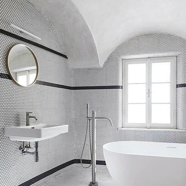 Modern bathroom with curved ceiling, hexagon tiles, freestanding tub, and round mirror.