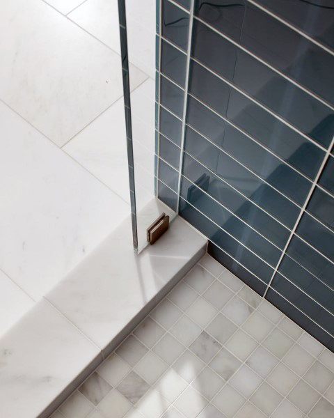 Navy blue beveled tile shower wall with white marble floor and glass enclosure.