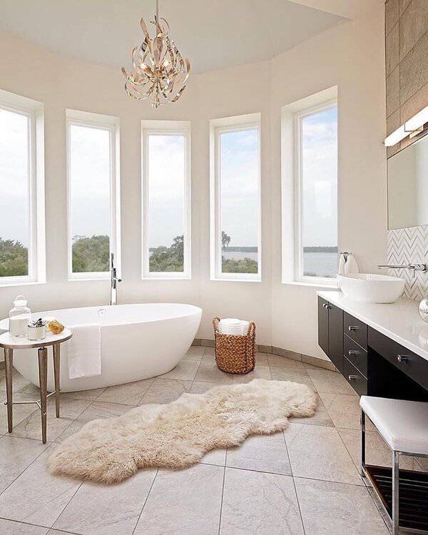 Swirl-inspired chandelier above a white freestanding tub, tall windows, plush rug, and sleek vanity in a bright, airy bathroom.