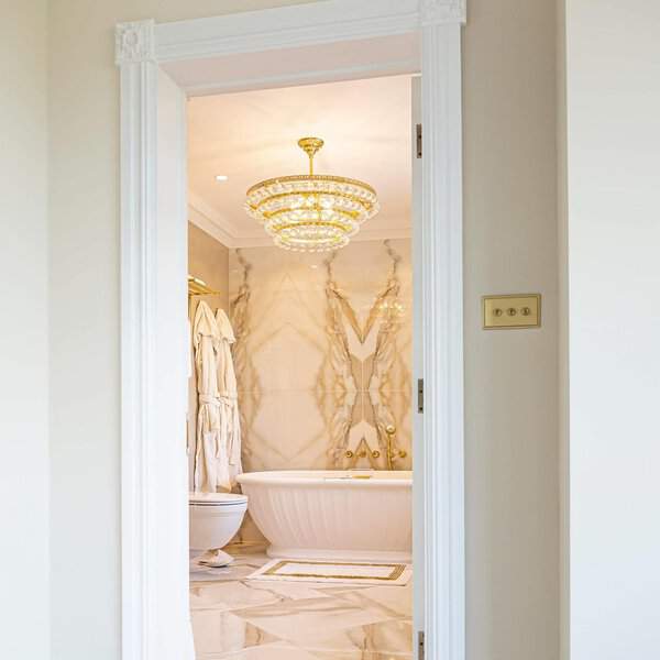 Tiered crystal chandelier with gold accents in a marble bathroom featuring a white fluted tub.