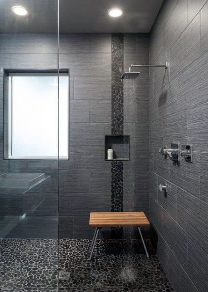 Dark travertine tile shower with pebble floor, vertical stone accent, and wooden stool.