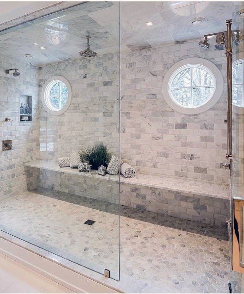 Spacious marble shower with round windows, built-in bench, and dual rainfall showerheads.