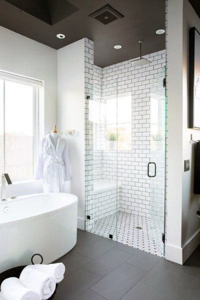White beveled subway tile shower with black grout, glass enclosure, and freestanding bathtub.